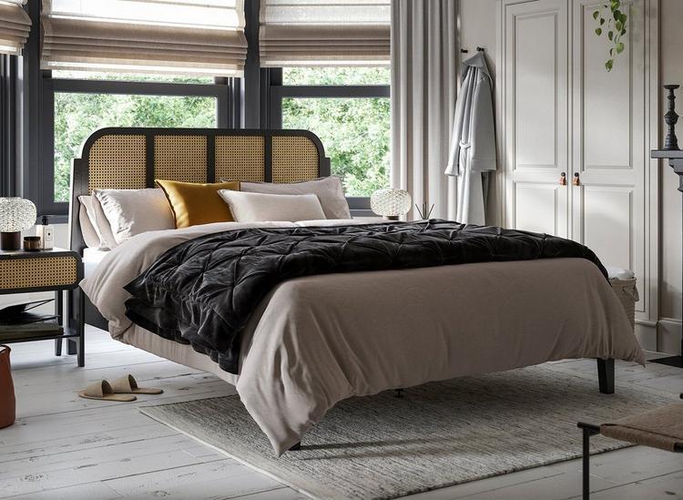 Black wooden and rattan bed frame, styled with matching bedside tables in a white bedroom.