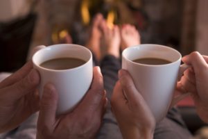 Two people holding two white mugs of coffee, while wrapped up in cosy loungewear.