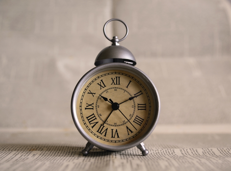 A silver and beige alarm clock on newspaper, against a brick wall