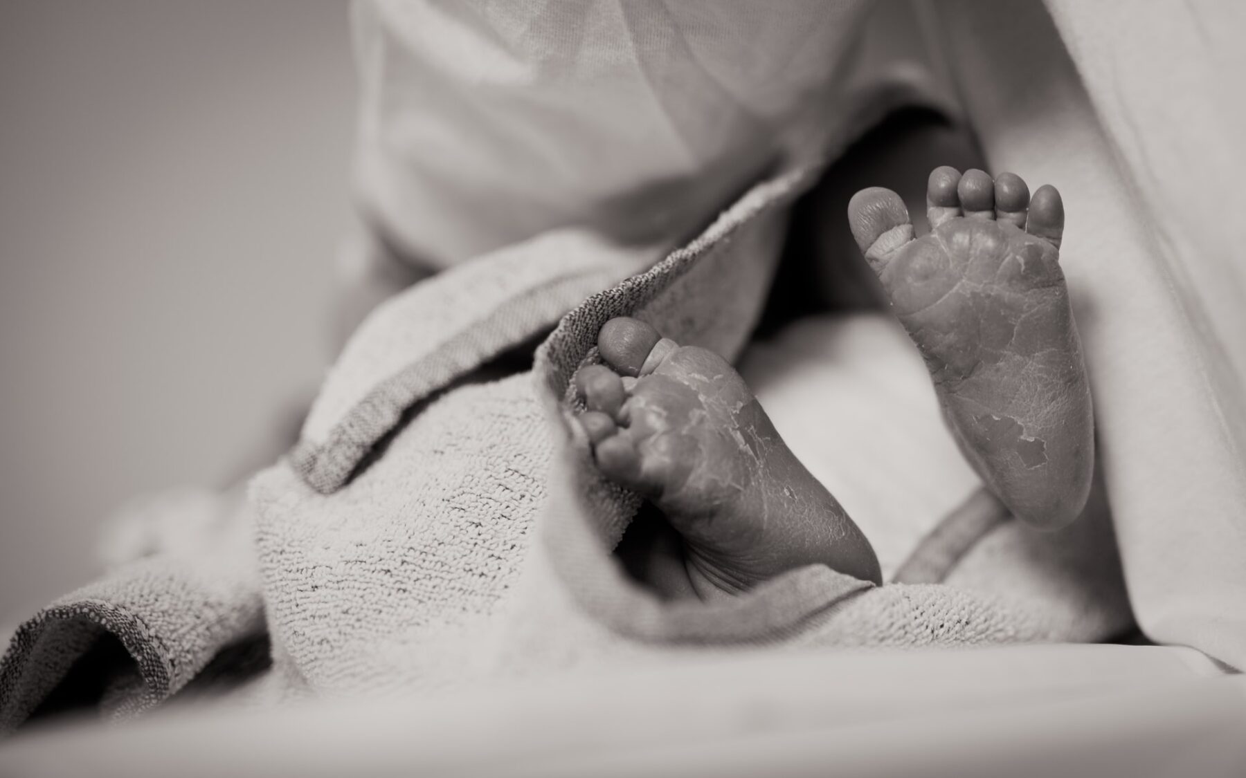 A baby's feet are visible, with the rest of the baby swaddled in blankets. The image is in greyscale.