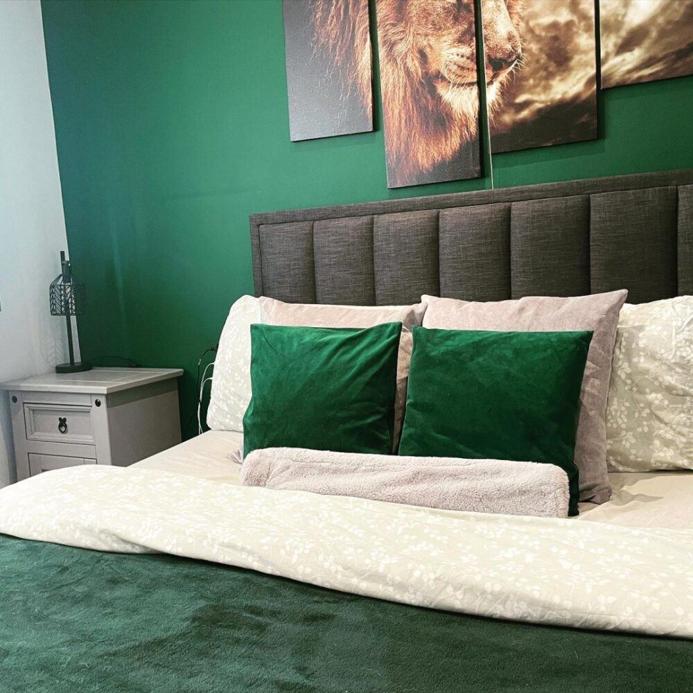 Bed with green and white bedding against green wall with artwork of a lion above