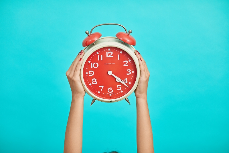 A white and red clock held up against a teal wall