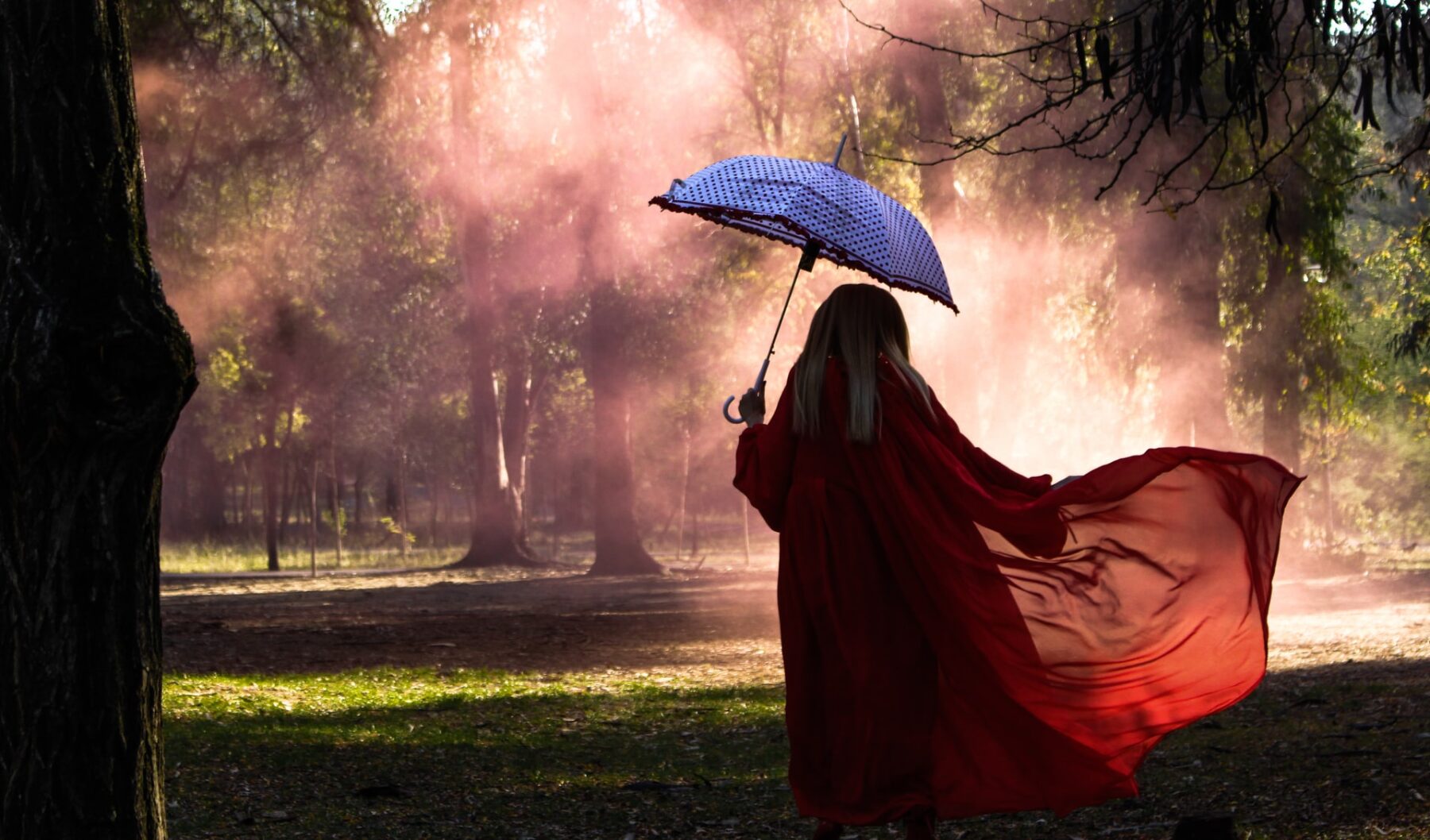 A fully veiled person walks through a rainy, yet sunny, forest with a blue umbrella.